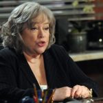 kathy-bates-sitting-at-a-desk-talking-to-an-off-screen-person-in-harrys-law.jpg